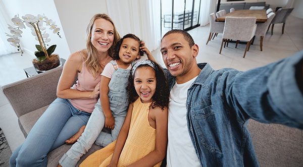 A young family of four takes a selfie on the couch inside their new home.